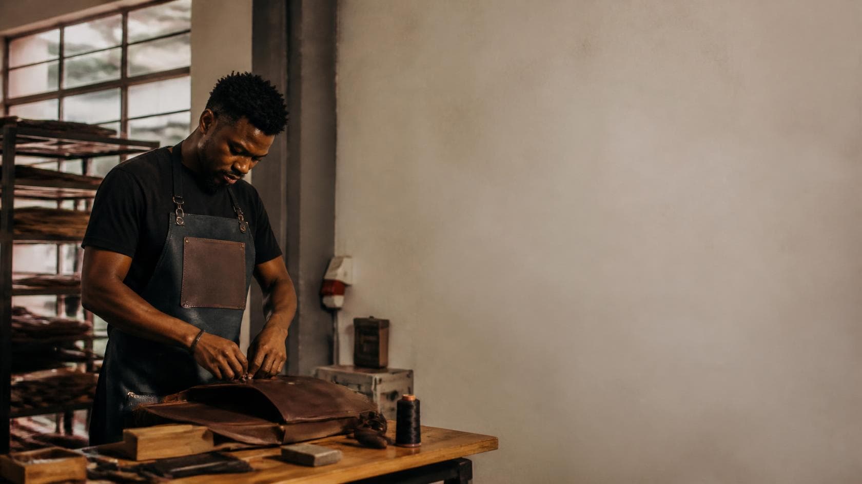 The owner of a small leather workshop finishing a bag at his bench